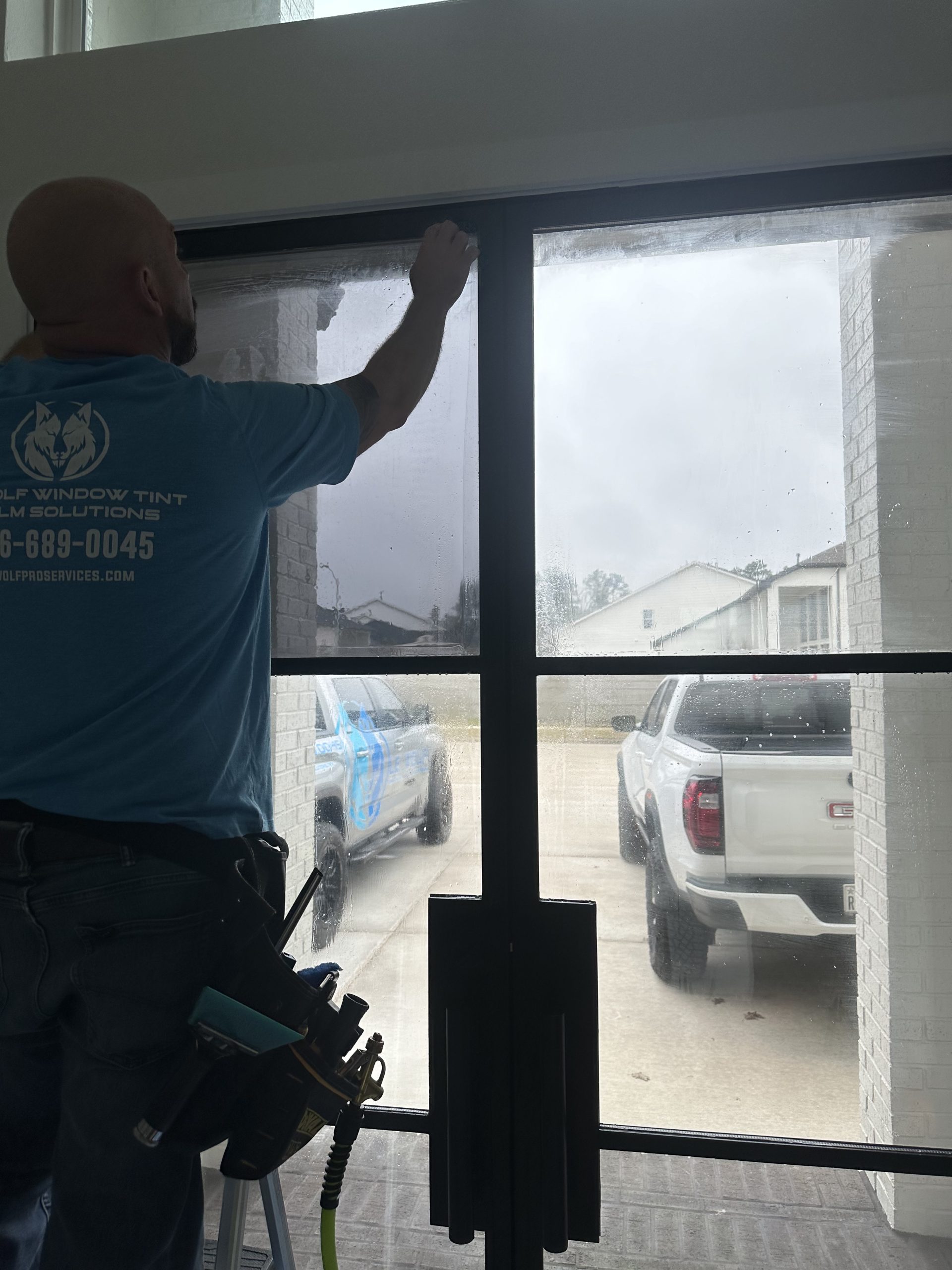 Window tinting technician applying film to a commercial window in Shenandoah, Texas, near Research Forest Drive.