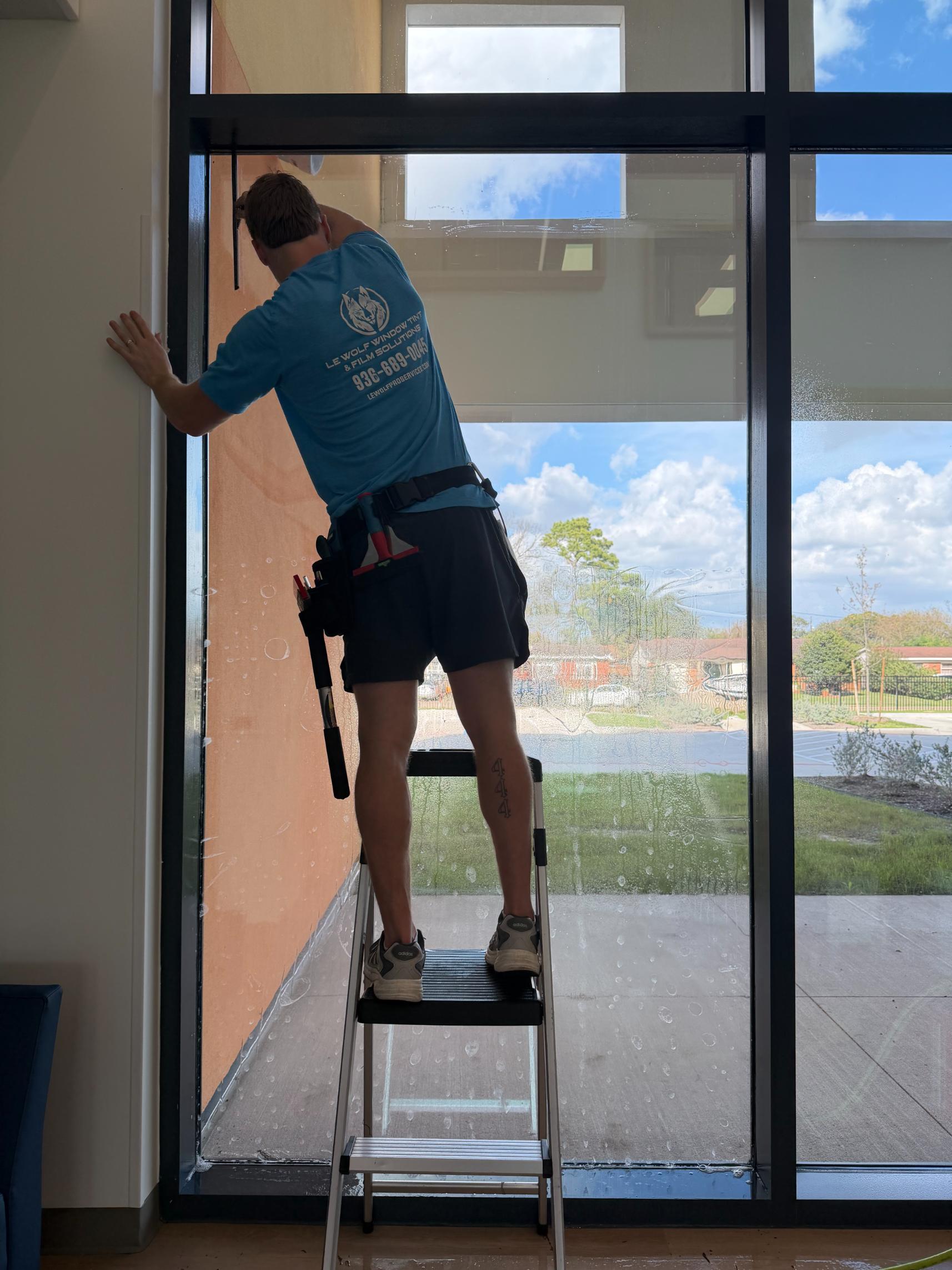 Window tinting technician applying film to a commercial building near the National Museum of Funeral History in
